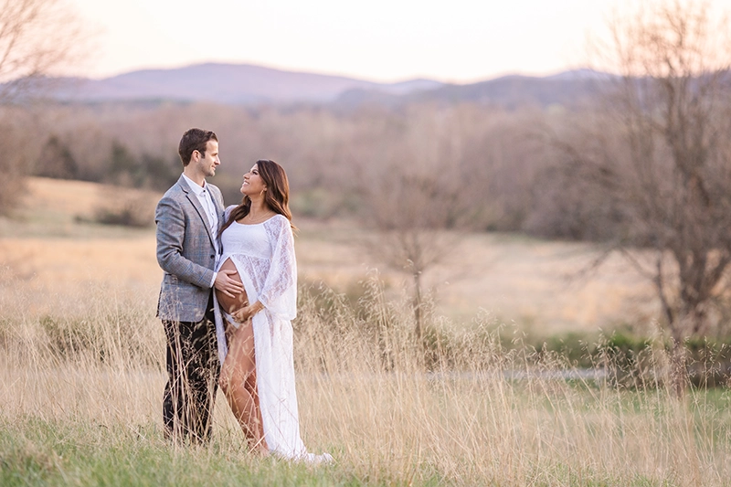 Couple posing for maternity portraits with mountains in the background at sunset.