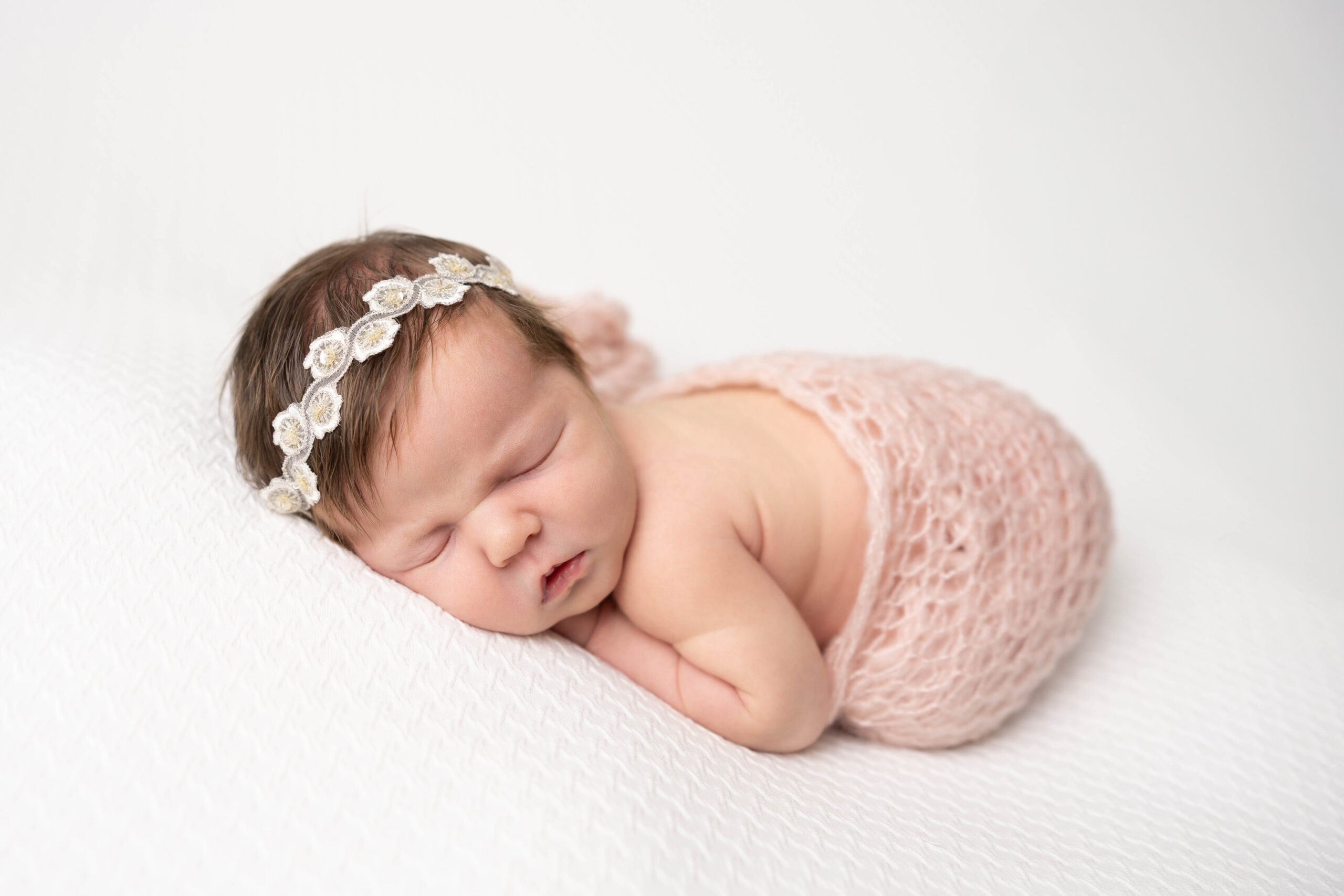 Newborn baby swaddled in a soft pink hand-knitted wrap, peacefully posed on a cozy blanket.