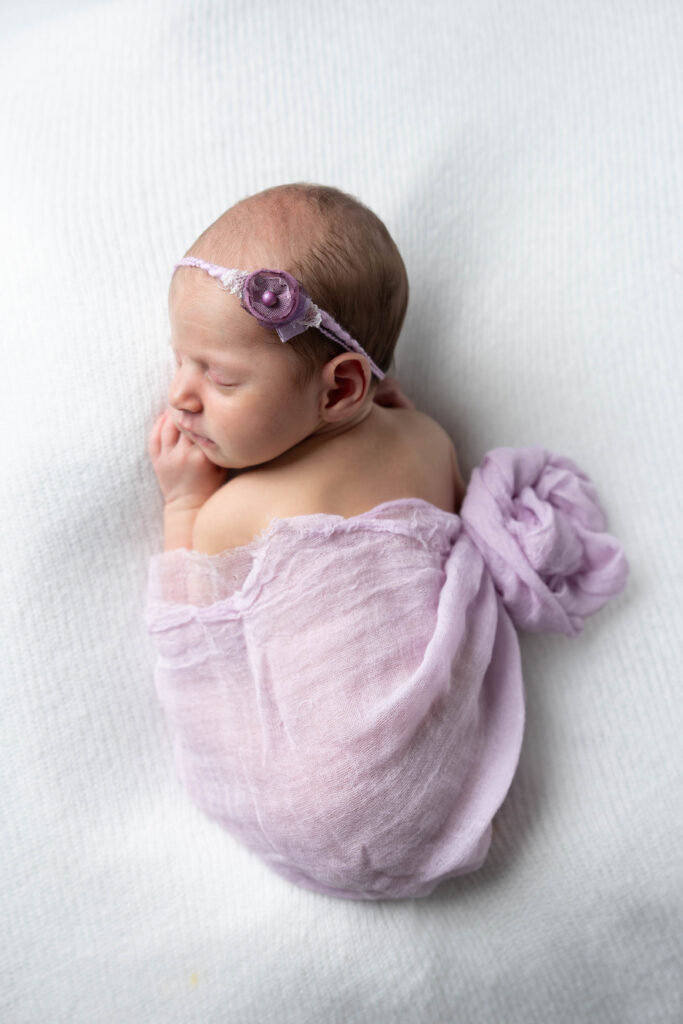 Newborn baby girl Sloane swaddled in a soft wrap, sleeping peacefully on a cozy blanket