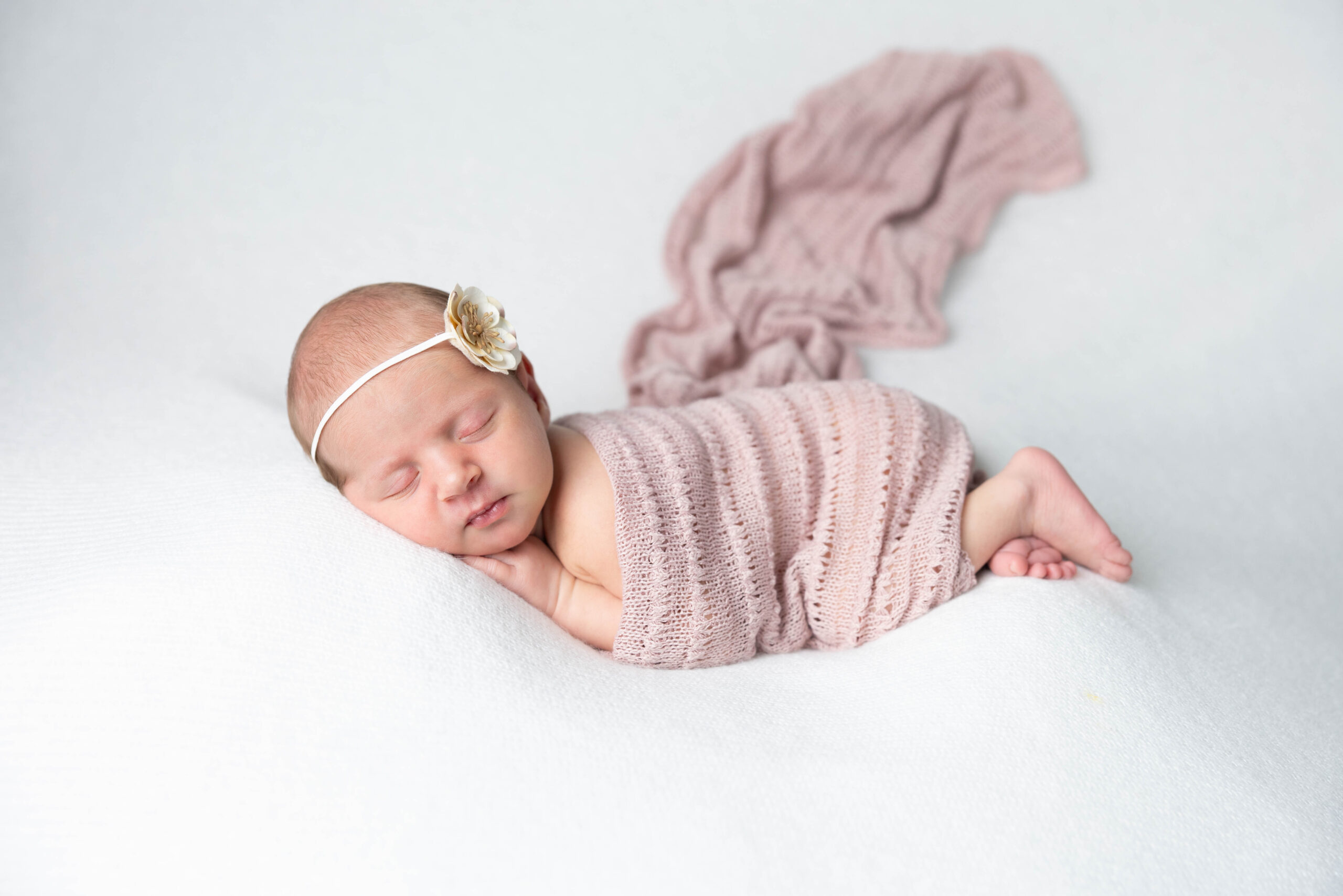 newborn baby sleeps swaddled in a blush wrap on a soft white blanket