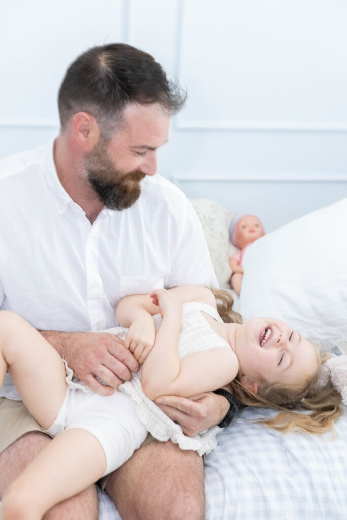 Big sisters jumping on the bed with newborn baby Taylor during an in-home lifestyle newborn photography session in Northern Virginia.