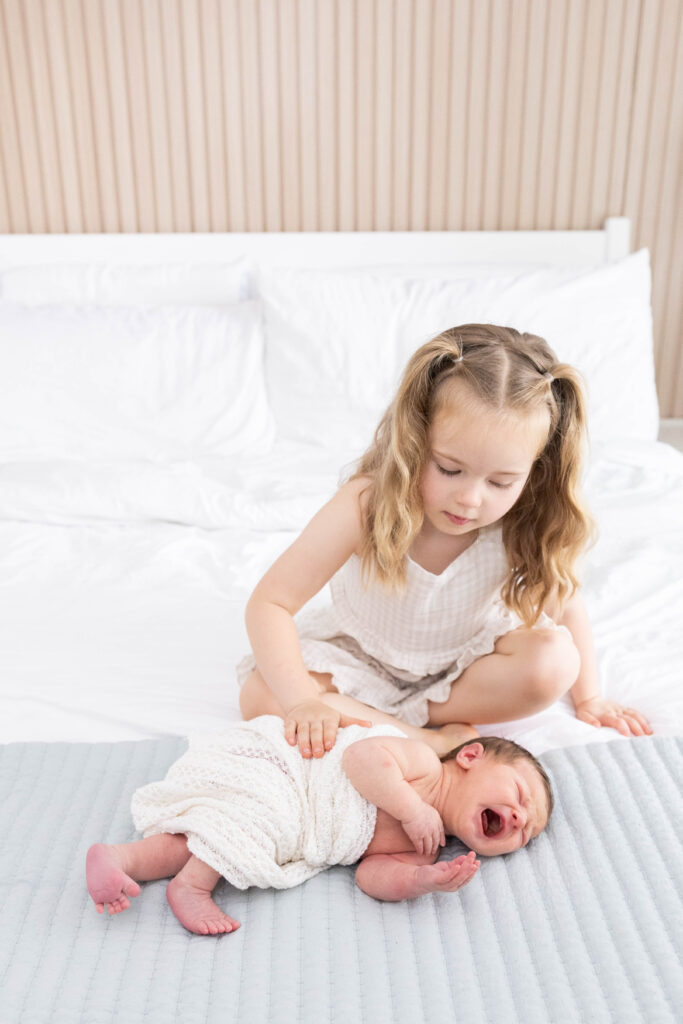 Big sisters jumping on the bed with newborn baby Taylor during an in-home lifestyle newborn photography session in Northern Virginia.